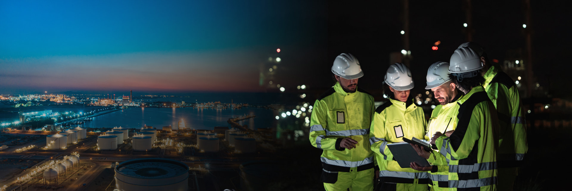 Energy project team in hi-vis gear reviewing plans above a lit refinery at night